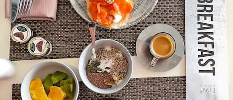 A breakfast setting with smoked salmon on toast, a bowl of mixed fruits, a bowl of seeds and nuts, a cup of coffee, and an omelette on a plate.