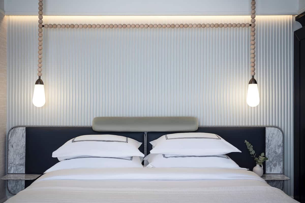 A neatly made bed with white linens, a dark headboard, and two bedside lamps.