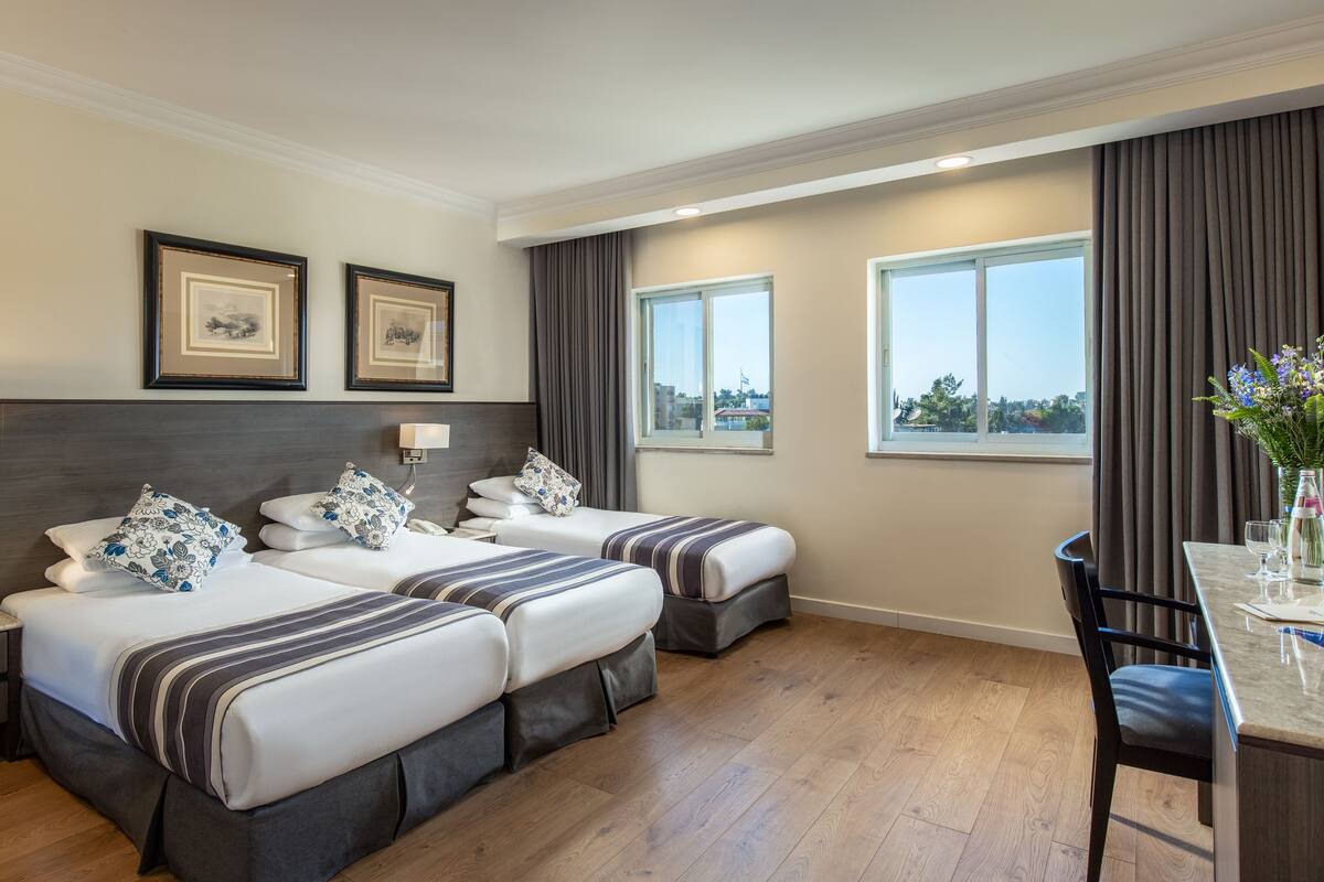 Ein Hotelzimmer mit zwei Betten, einem Schreibtisch und Blick auf die Stadt.