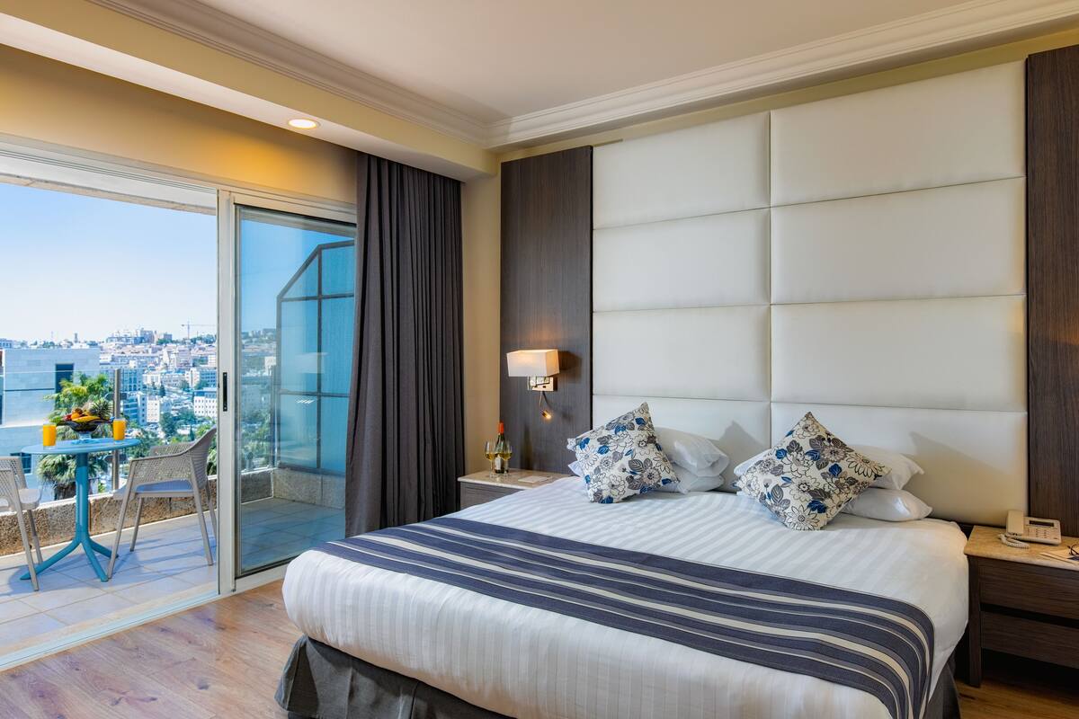 Ein modernes Hotelzimmer mit einem großen Bett, einem Balkon mit Blick auf die Stadt und einer Glastür zum Balkon.