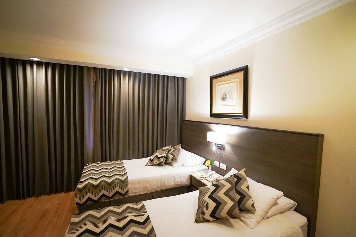 Ein Hotelzimmer mit zwei Betten, einem gerahmten Bild an der Wand und einem Vorhang vor dem Fenster.