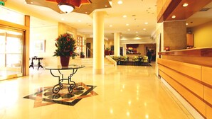A spacious lobby with a reception desk, a staircase, and a large potted plant. - Ambassador Hotel (Jerusalem)