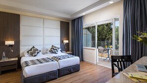 A hotel room with a large bed, a desk with a laptop, and a balcony with a table and chairs. - Ambassador Hotel (Jerusalem)