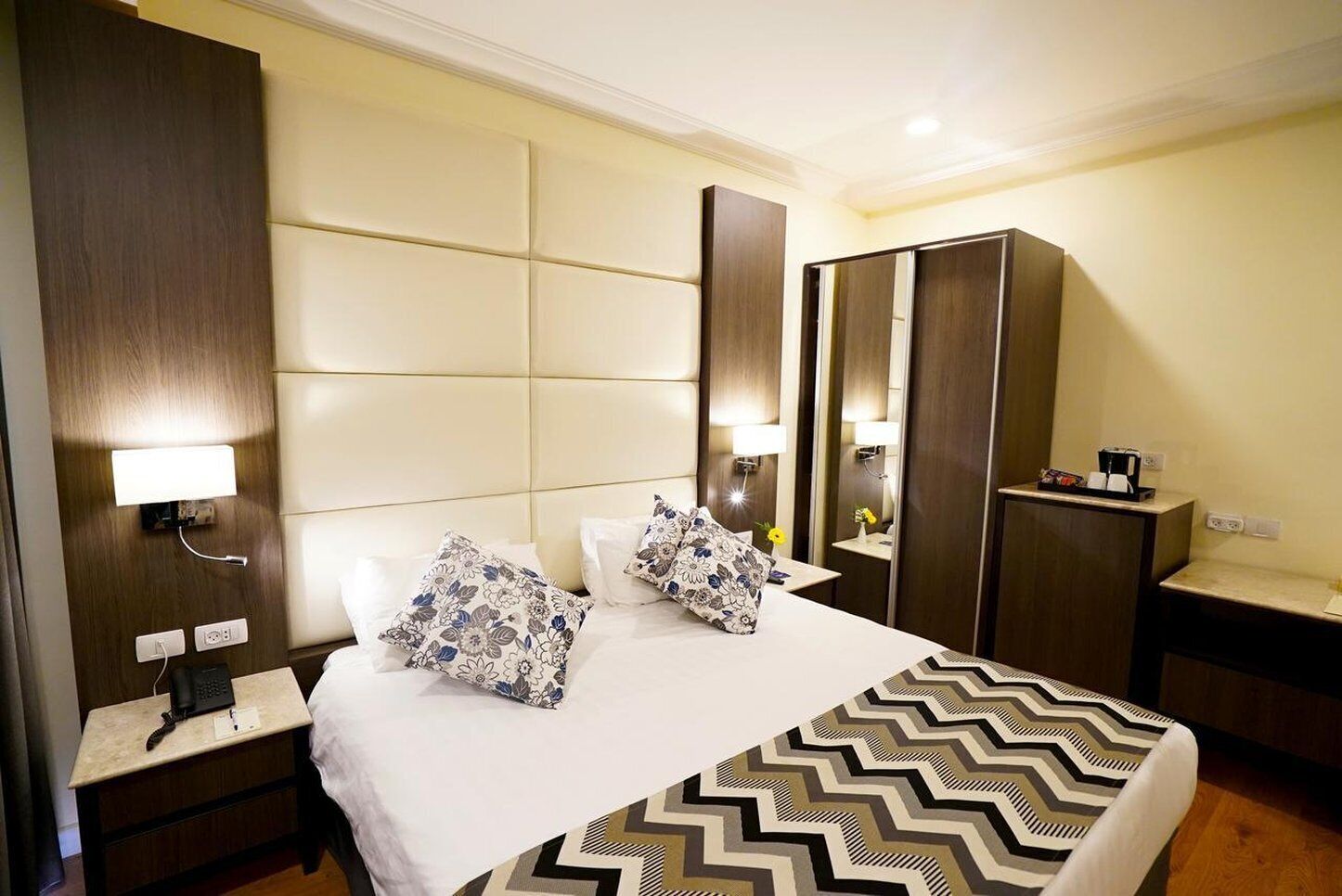 Habitación de hotel con una cama grande, dos mesitas de noche, un armario y un escritorio con lámpara.