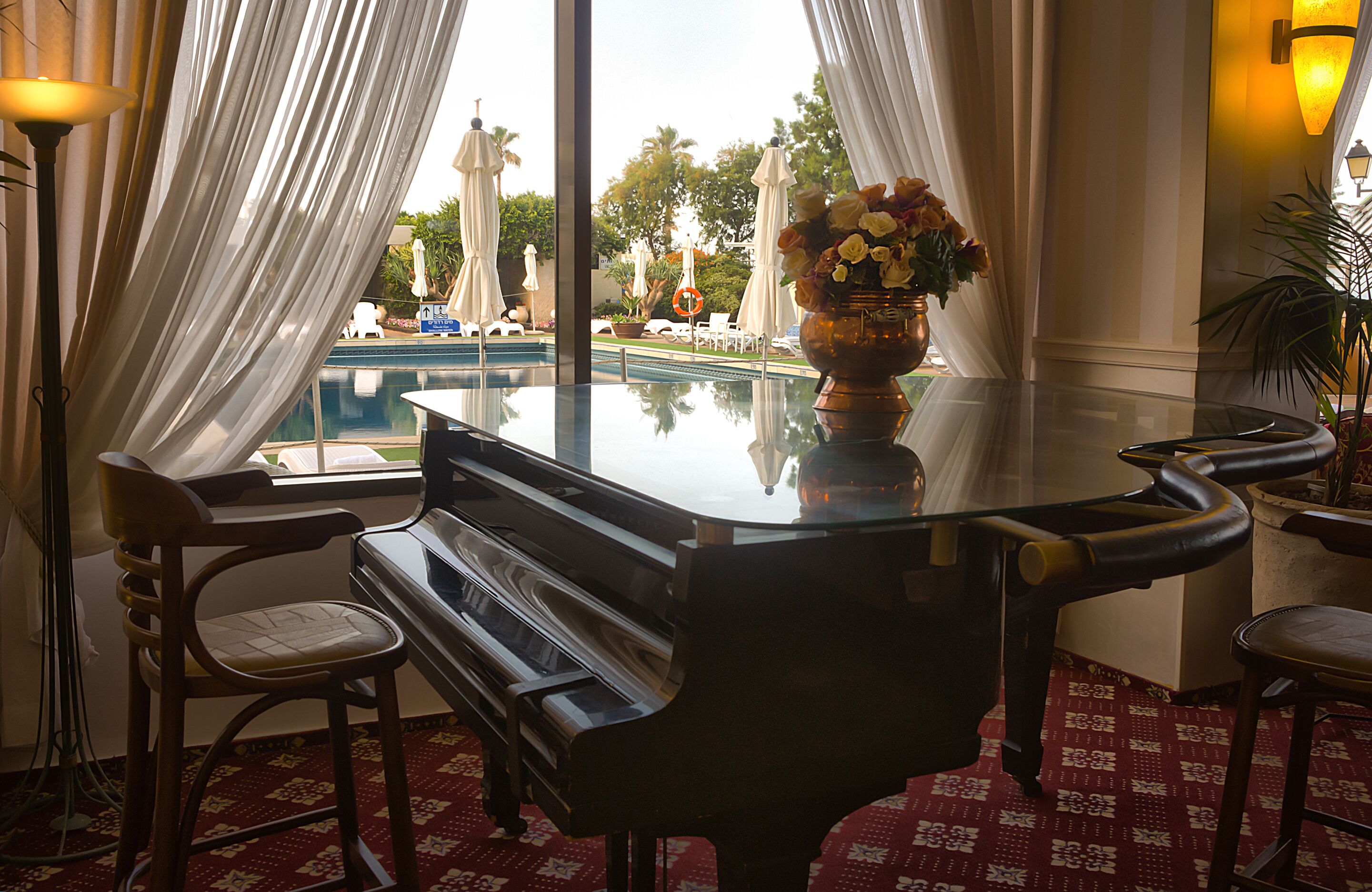 Un piano dans une pièce donnant sur une piscine et des parasols d’extérieur.