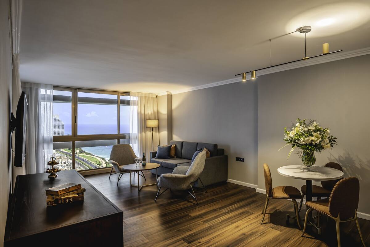 A modern living room with a sofa, chairs, a dining table, and a view of the ocean.
