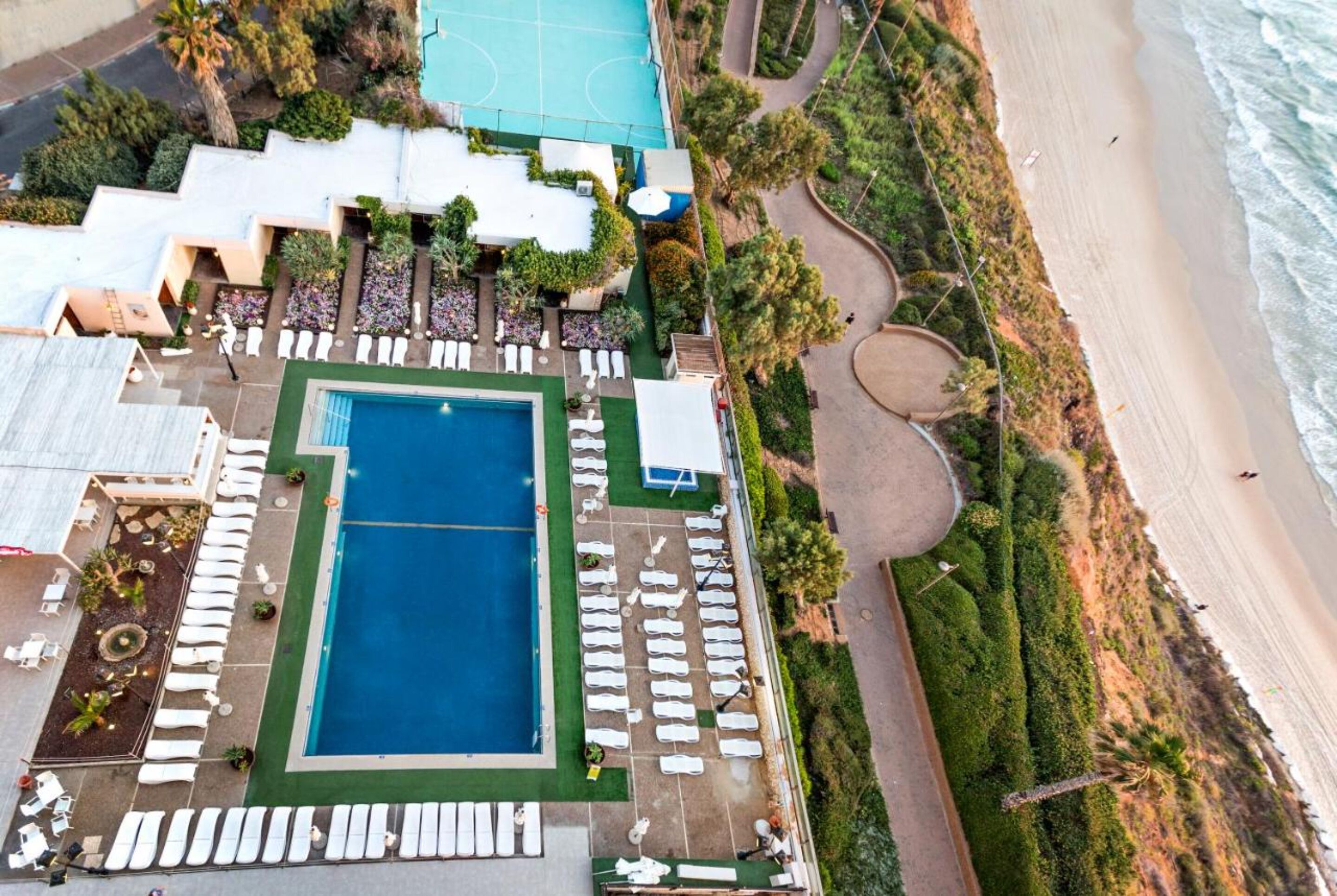 Vista aérea de un resort con piscina, tumbonas y playa.