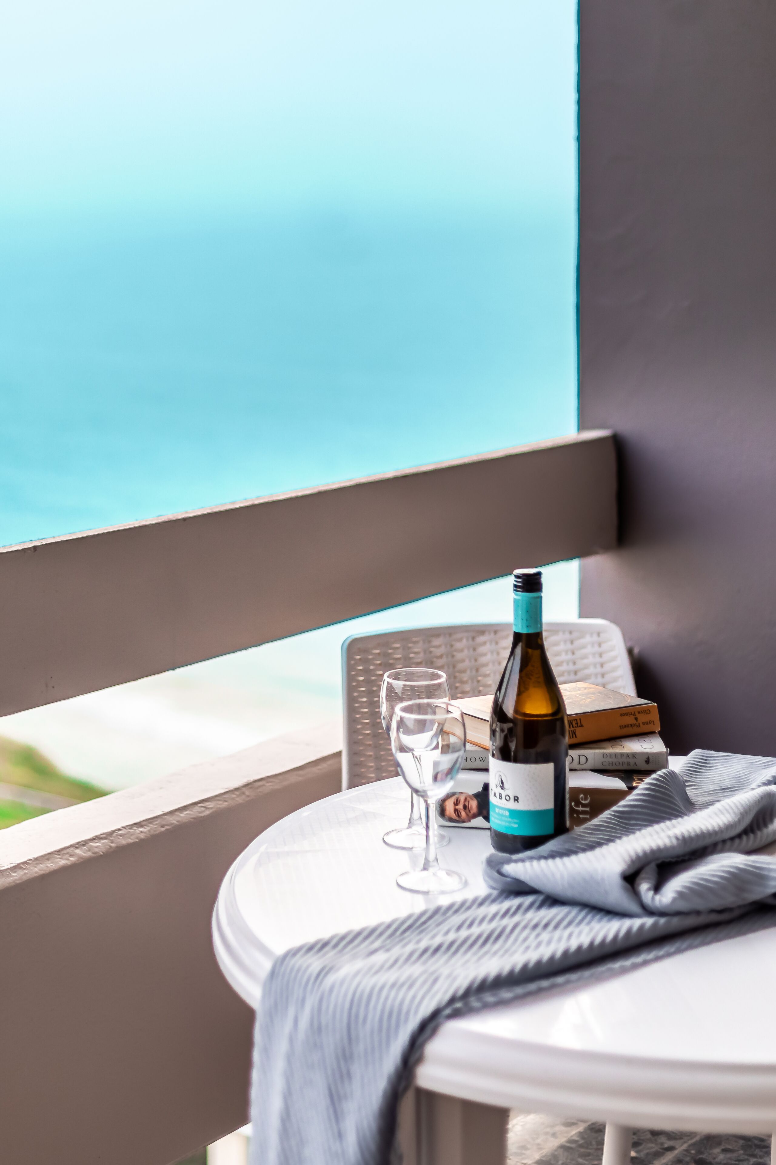 A balcony with a table, a bottle of wine, glasses, and books.