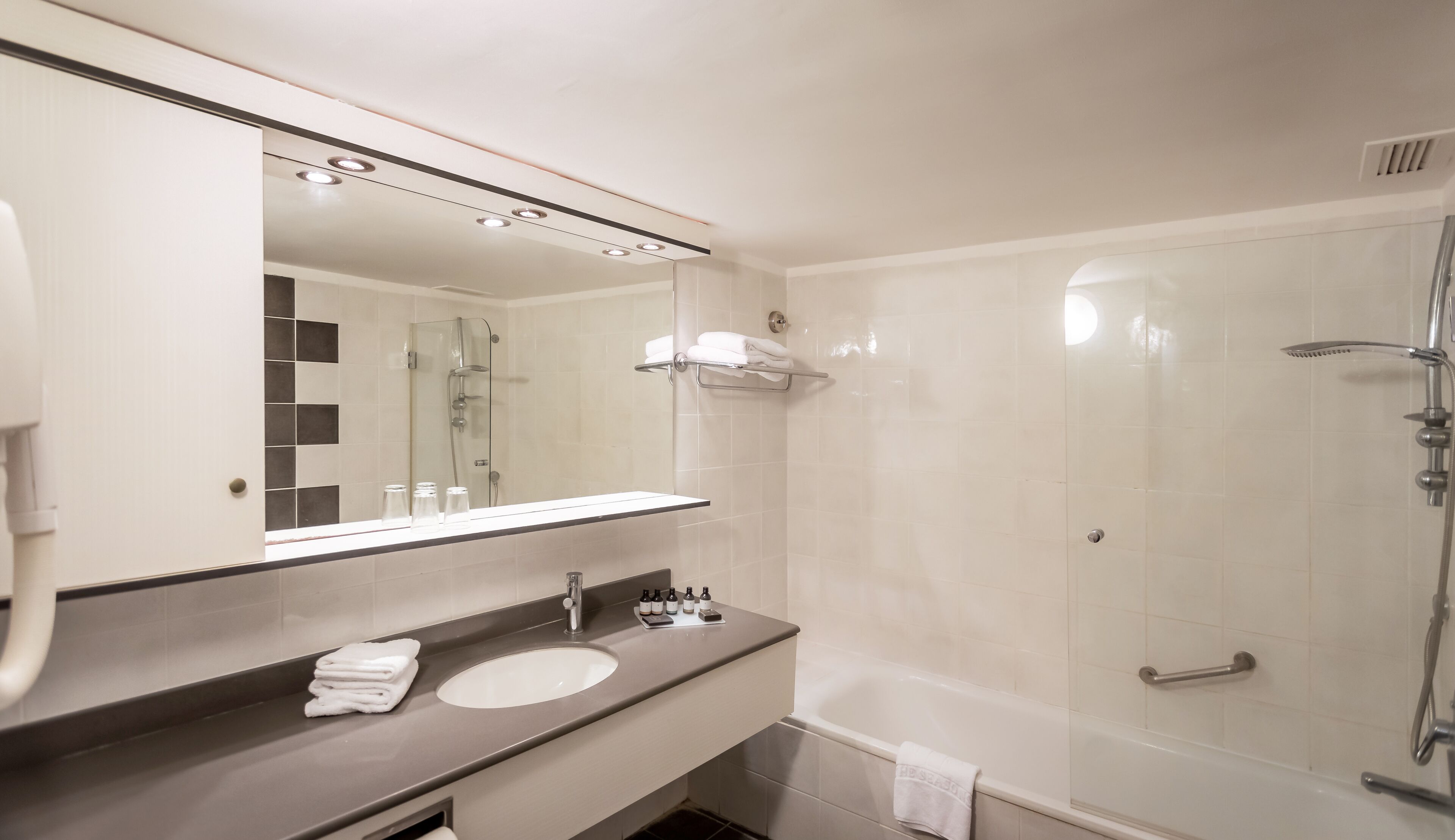 A modern bathroom with a large mirror, a sink, a shower, and a towel rack.