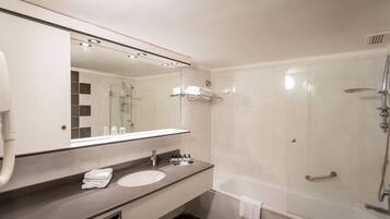 A modern bathroom with a large mirror, a sink, a shower, and a towel rack.