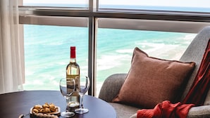 Una habitación con vista al océano, una mesa con una botella de vino, copas y un cuenco de frutos secos.
