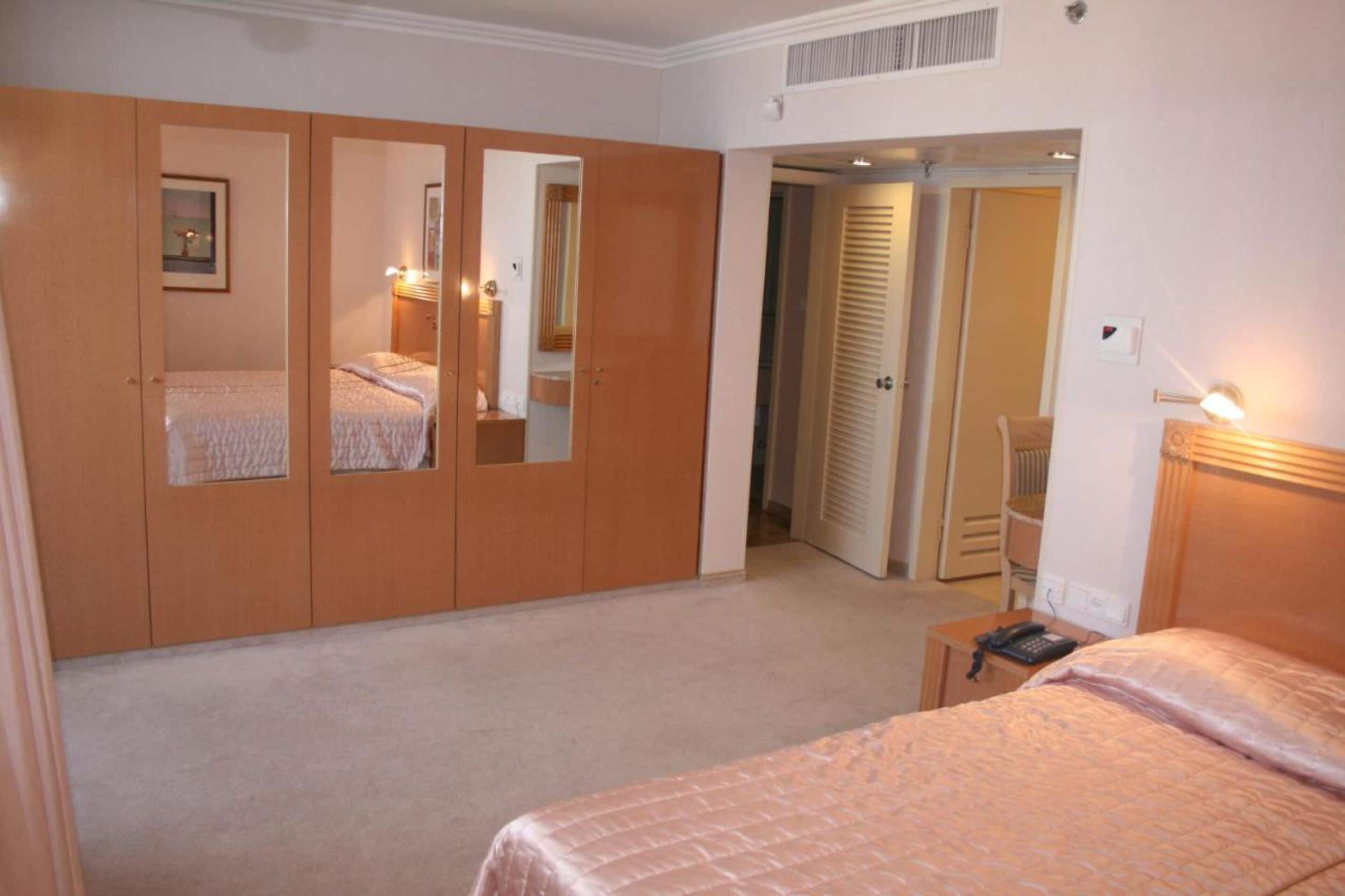 Un dormitorio con cama, armario, espejo y mesita de noche con lámpara.