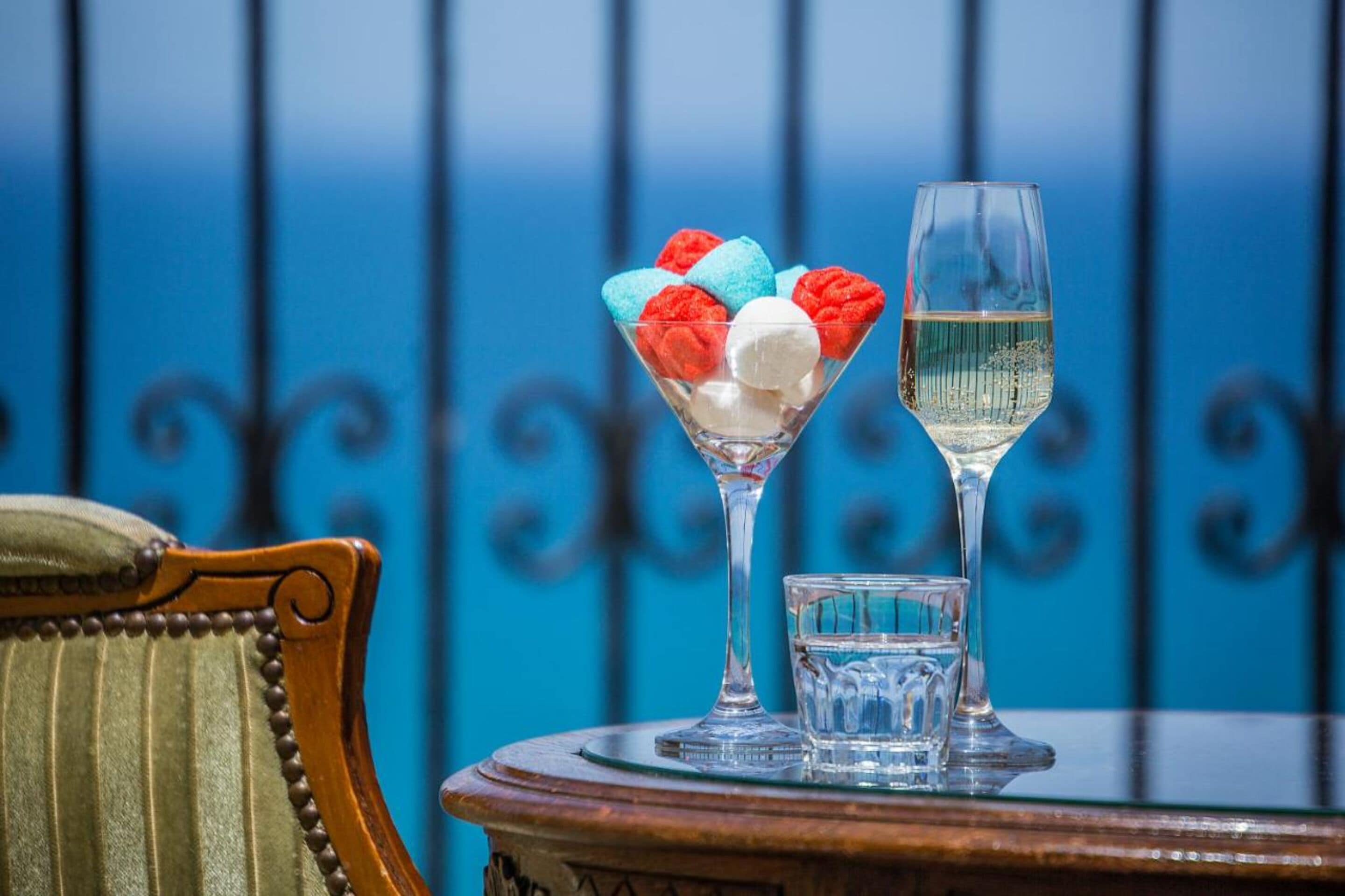 A table with a martini glass and a wine glass, a small glass, and a bowl of colorful marshmallows.