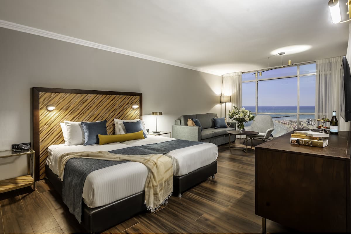 A hotel room with a large bed, a sofa, a desk, and a view of the ocean.