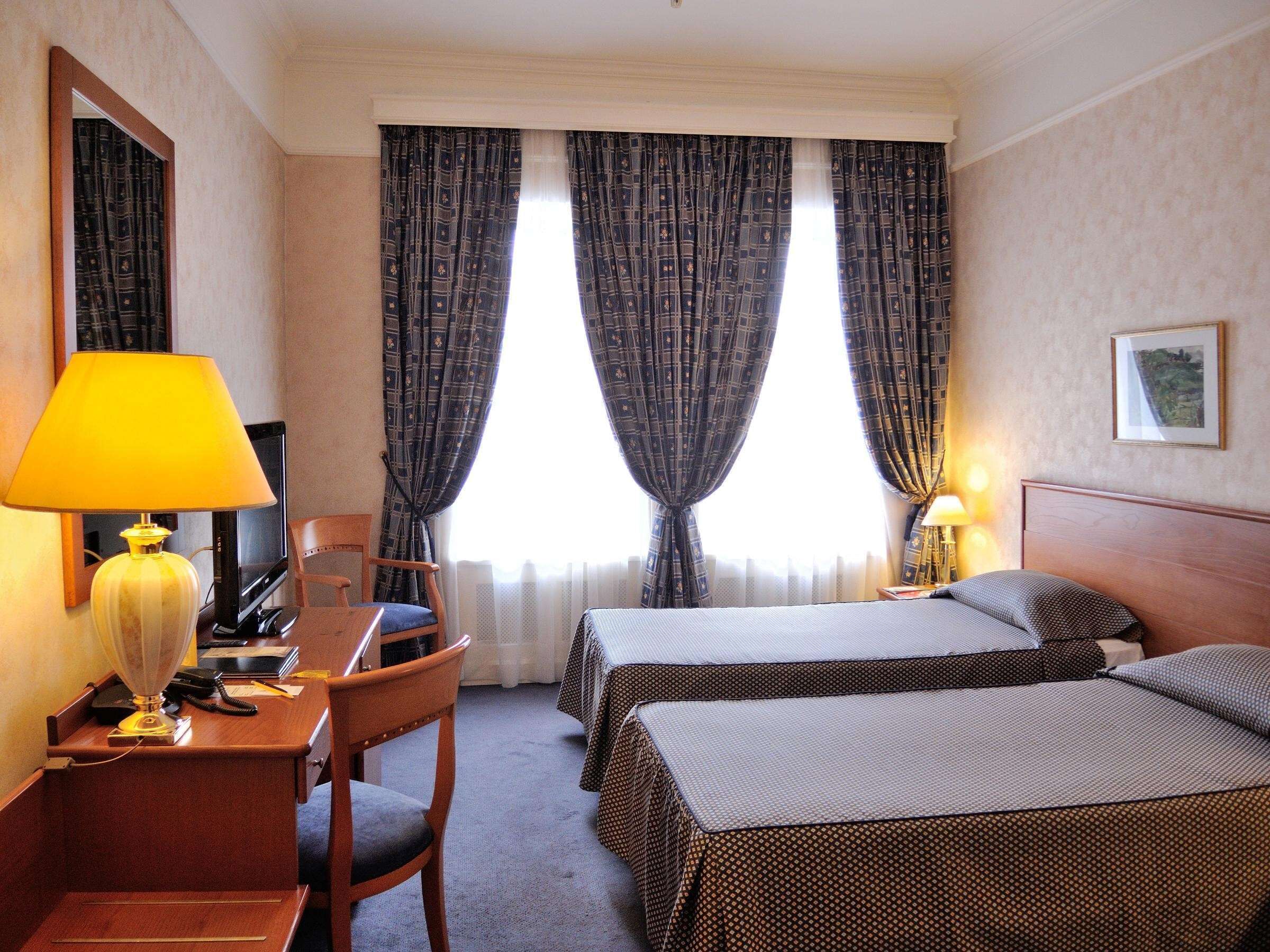 A hotel room with two beds, a desk with a chair, a lamp, and a television.