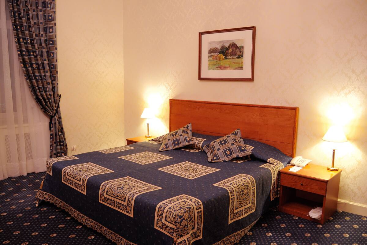 A neatly made bed with a patterned bedspread, two bedside lamps, and a framed picture on the wall.