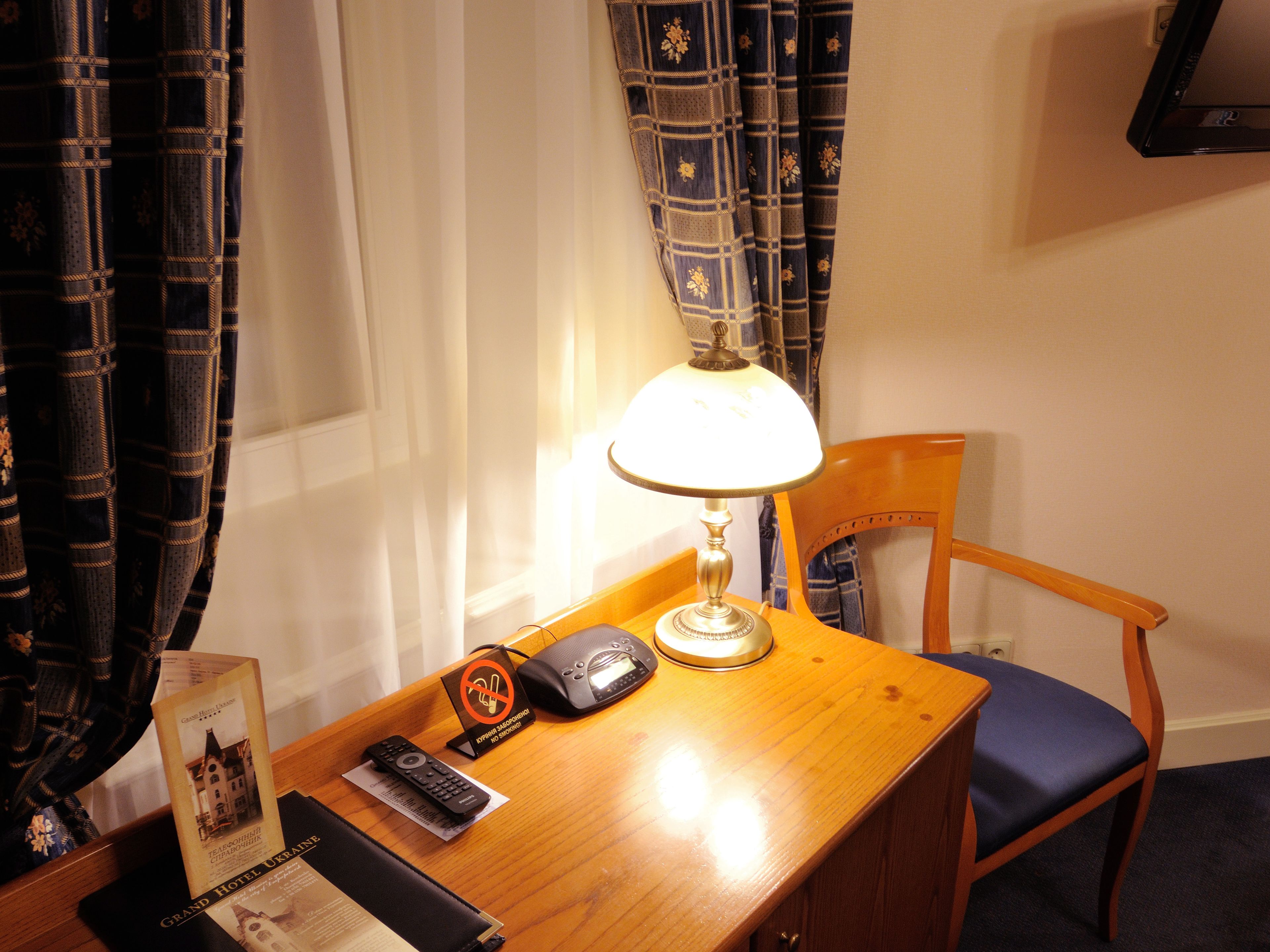 Habitación de hotel con escritorio de madera, lámpara, silla, control remoto y un letrero que indica prohibido fumar.
