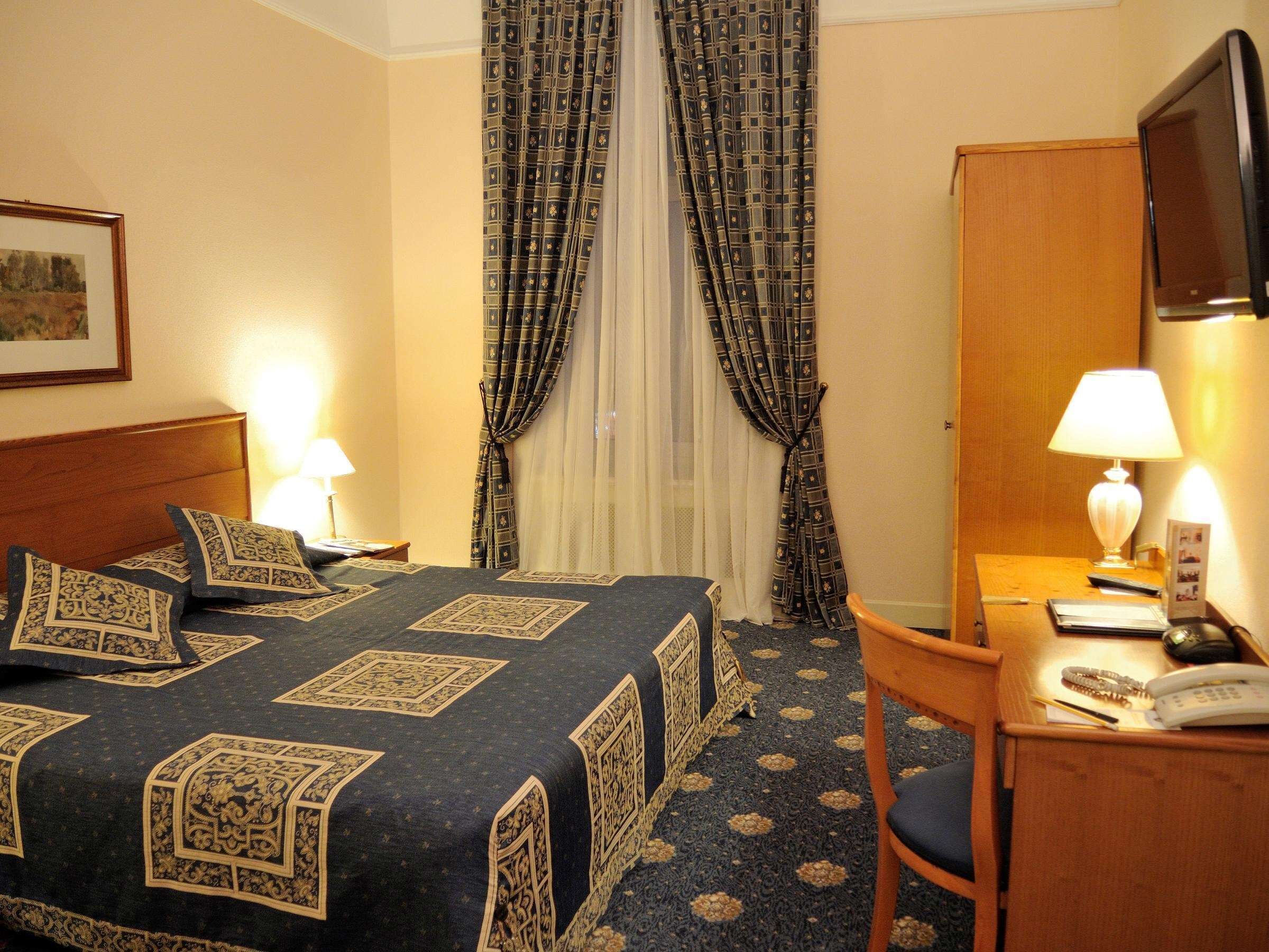 Una habitación de hotel con cama, escritorio, silla, televisor y cortinas.