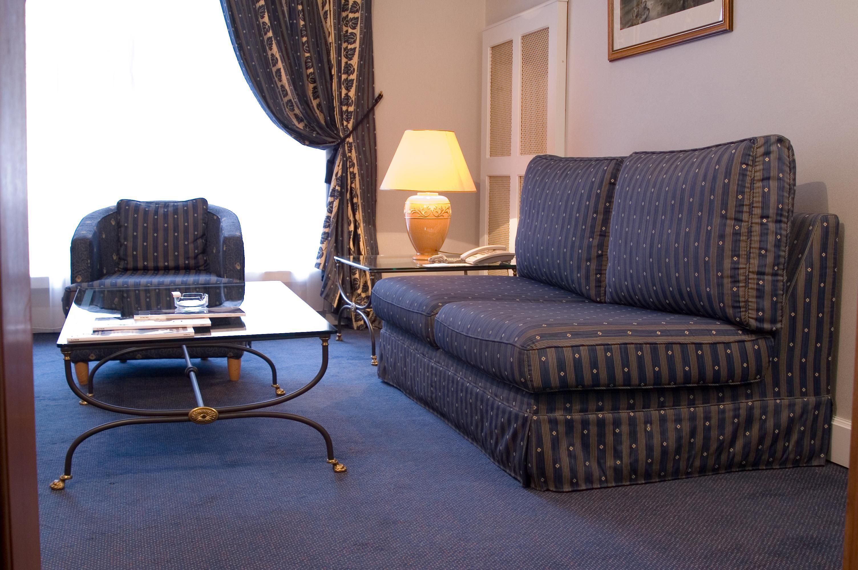 A room with a sofa, armchair, and a table with a lamp.