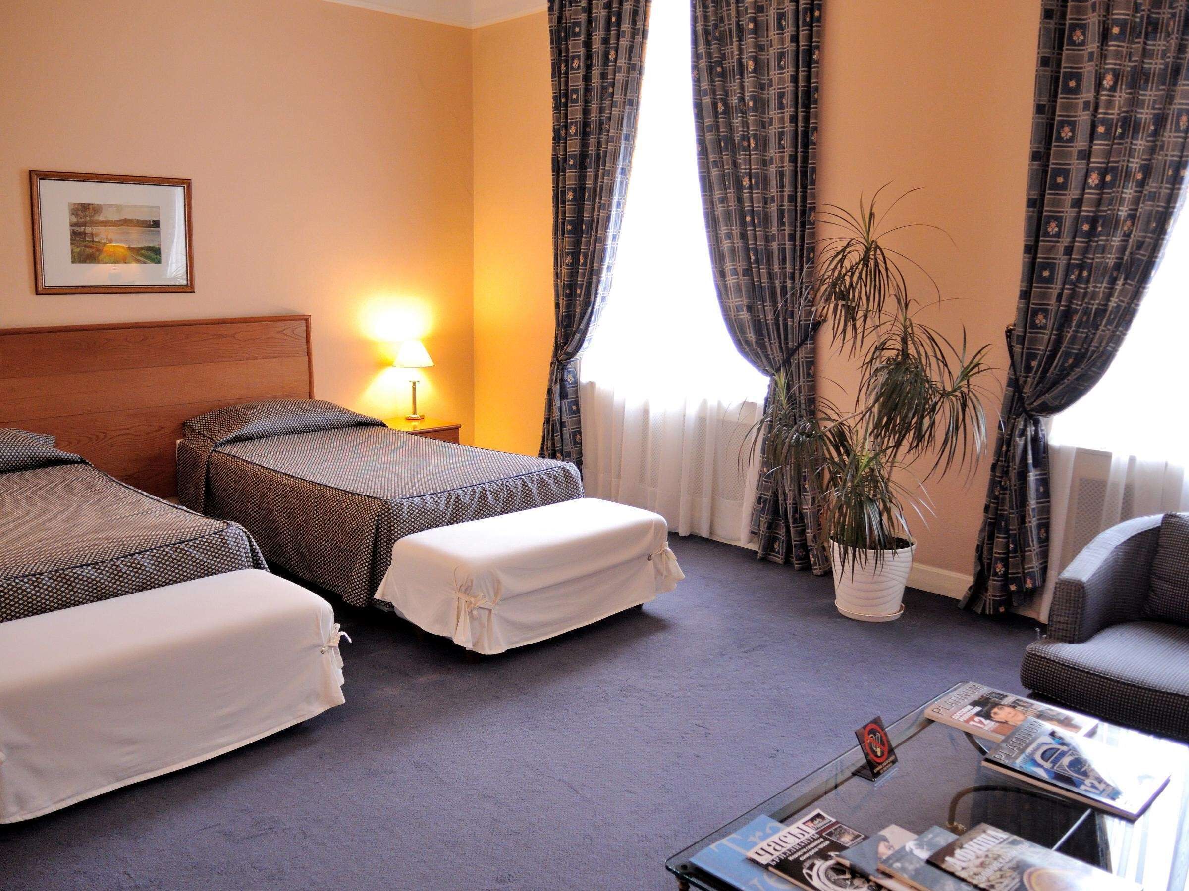 A hotel room with two beds, a sitting area, a table with magazines, and a potted plant.