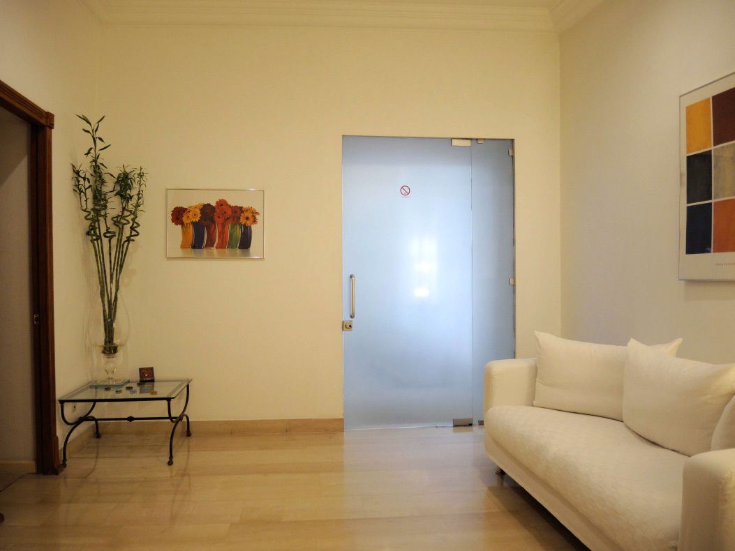 A living room with a white sofa, a glass coffee table, a framed floral artwork, and a door with a 'no entry' sign.