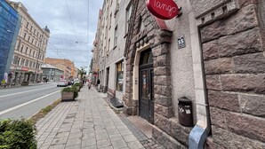 Vista de la calle con un edificio que muestra un letrero 'Tango', fachada de piedra y un contenedor de basura.