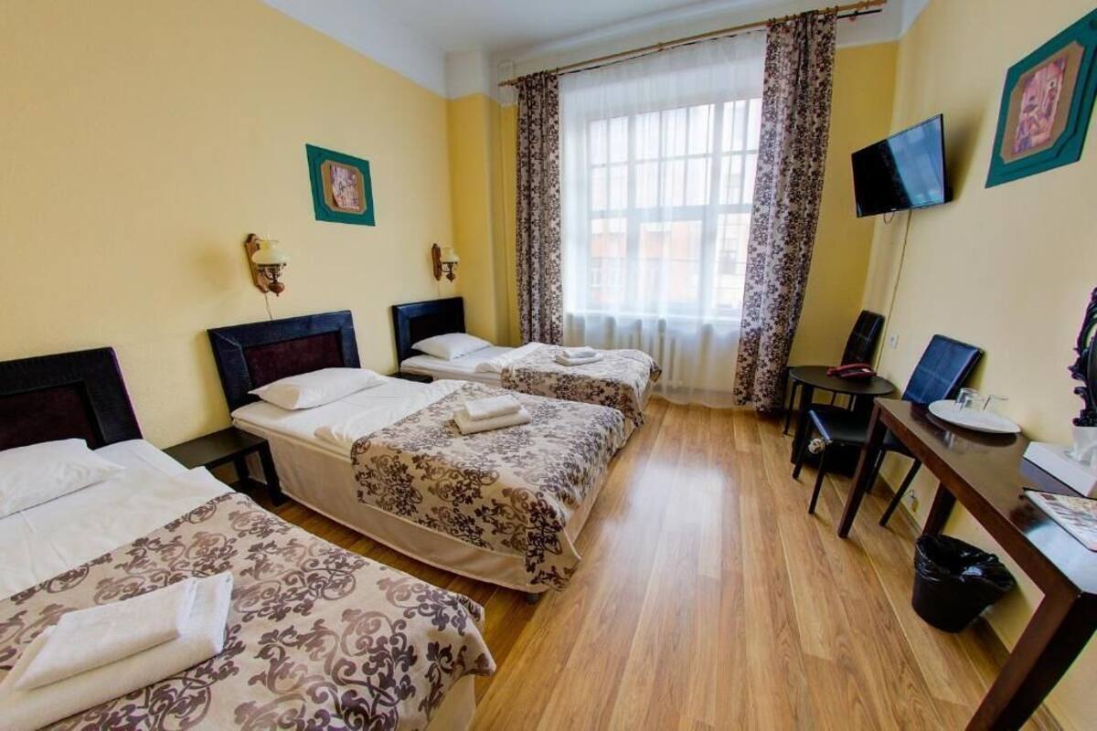 A hotel room with three beds, a desk, a chair, a television, and a window with curtains.