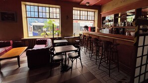 Zona de bar con barra, taburetes y área de estar con mesas y sillas.