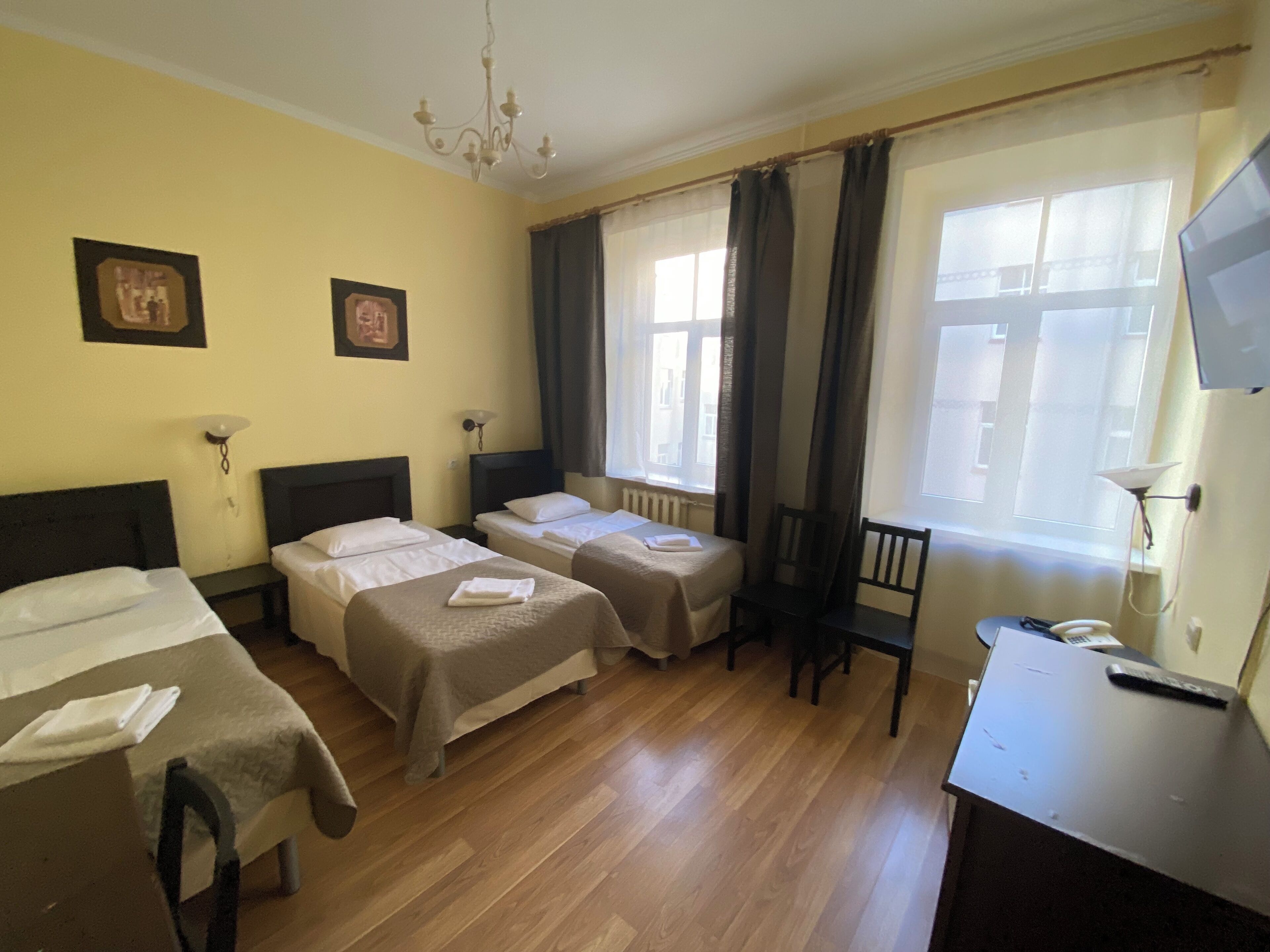 A hotel room with two beds, a desk, a chair, a TV, and a window with curtains.