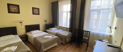 A hotel room with two beds, a desk, a chair, a TV, and a window with curtains.