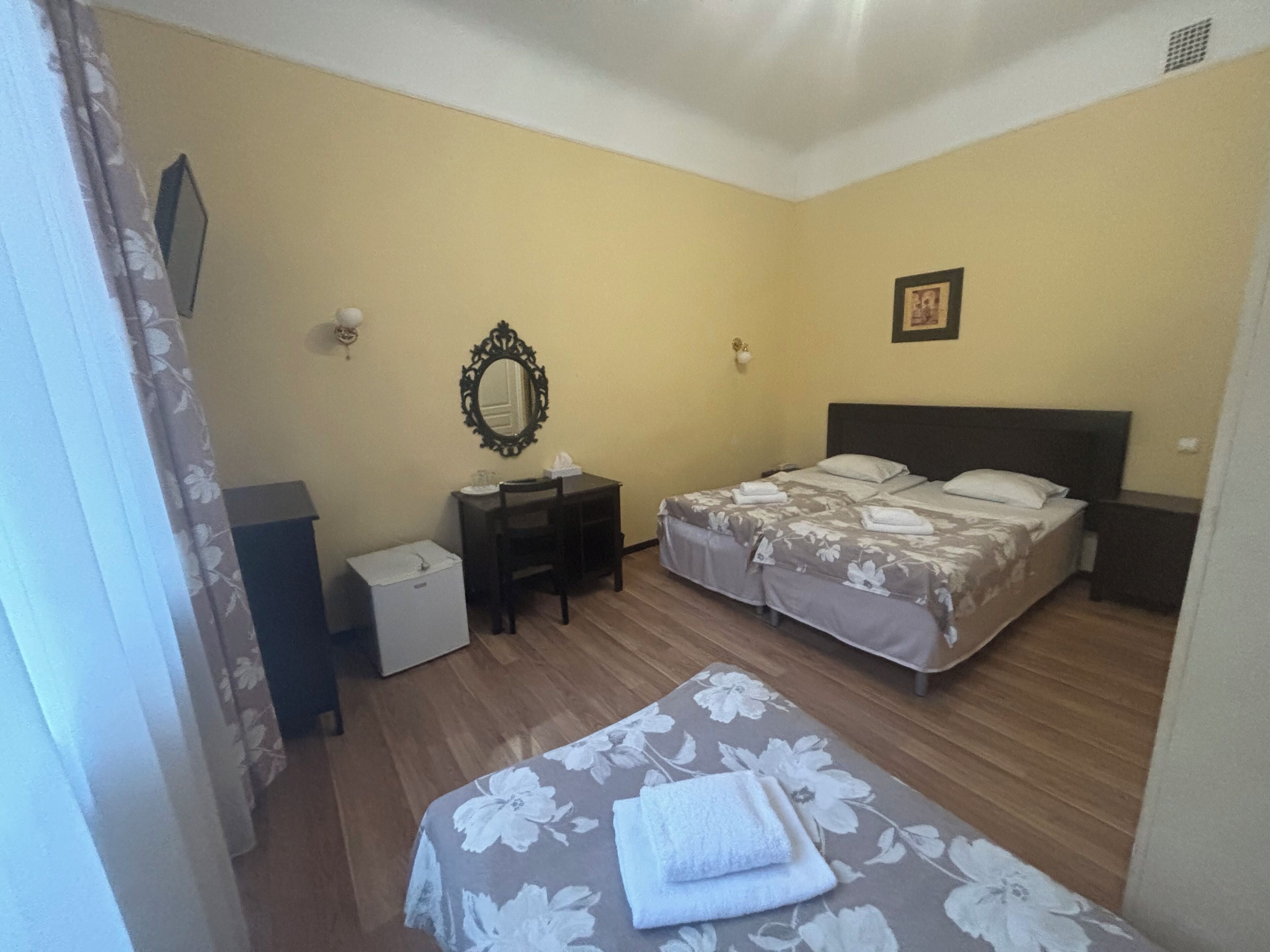 Una habitación de hotel con dos camas, un escritorio, una silla, un espejo y un armario blanco pequeño.