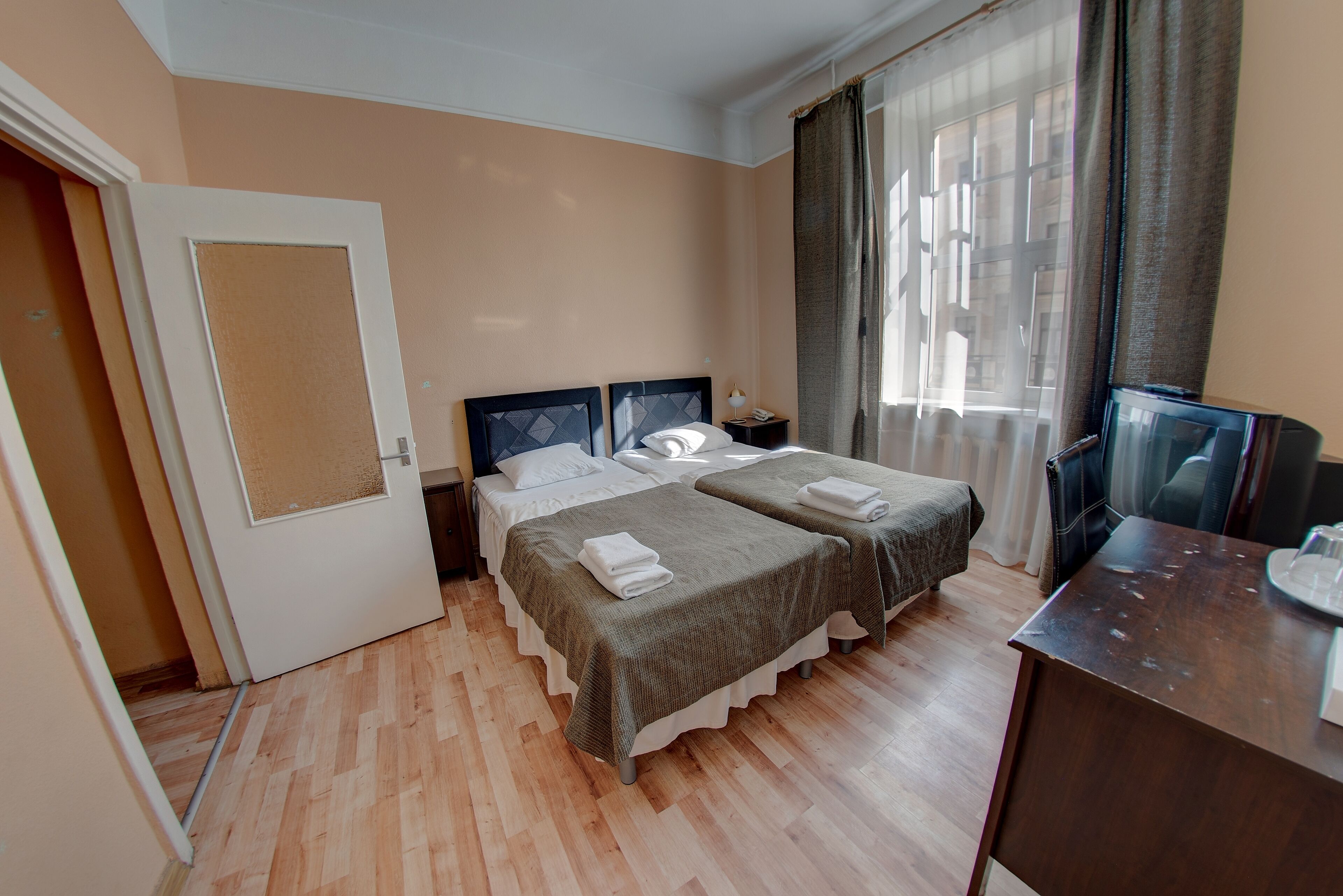 Habitación de hotel con dos camas, un escritorio, una silla, un televisor y una ventana con cortinas.