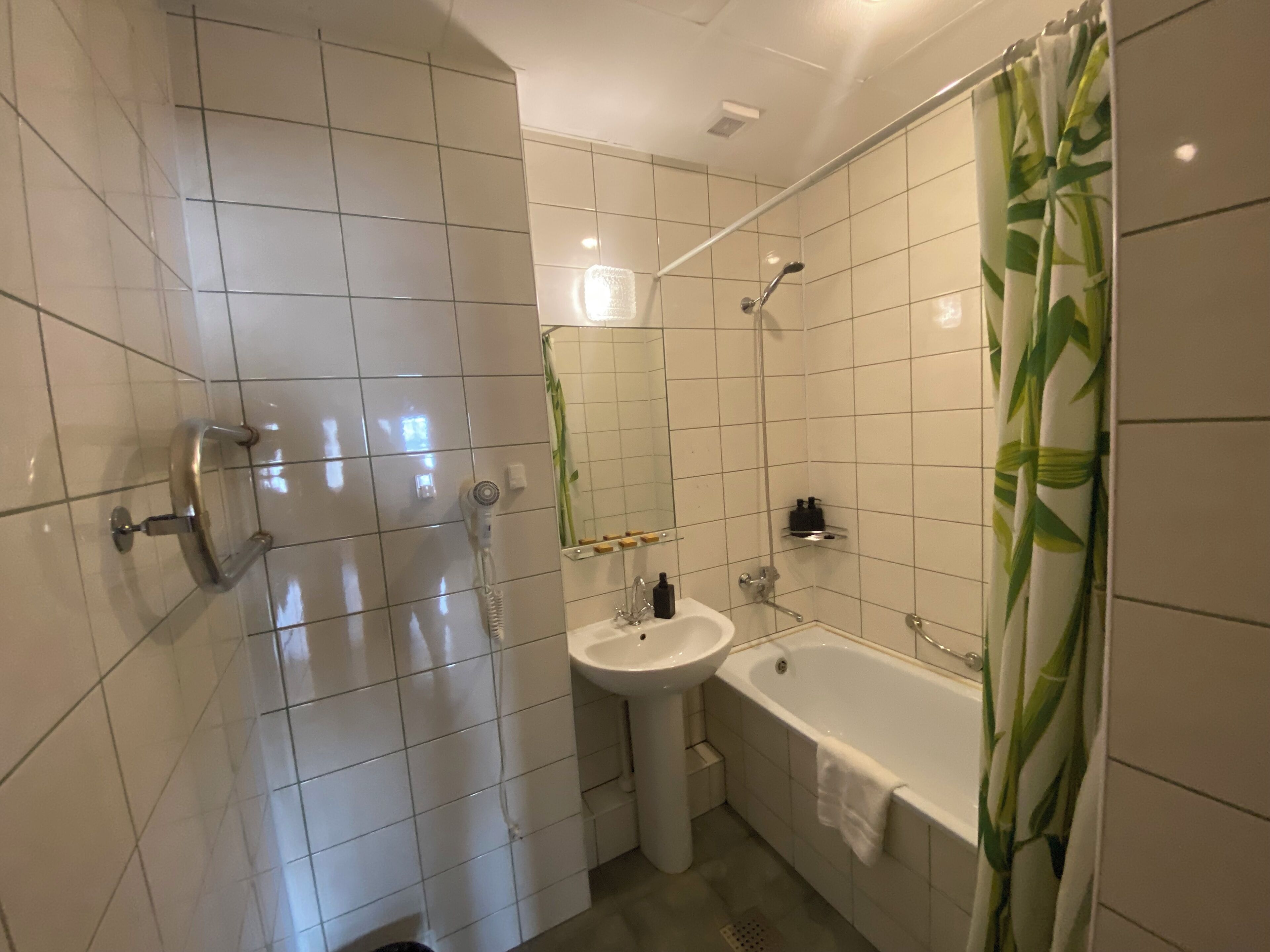 A modern bathroom with white tiles, a bathtub, a sink, and a shower.
