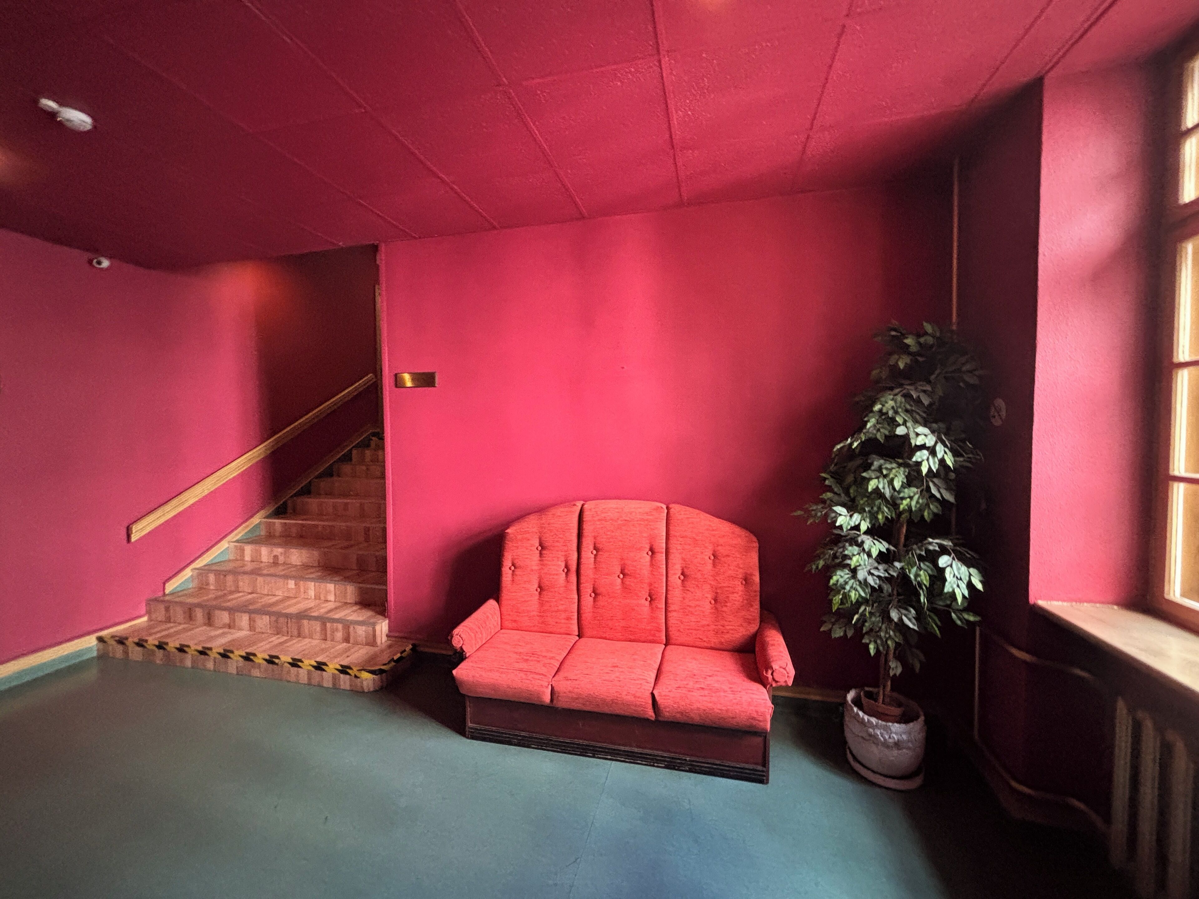 Una habitación con un sofá rojo, una escalera y una planta en maceta.