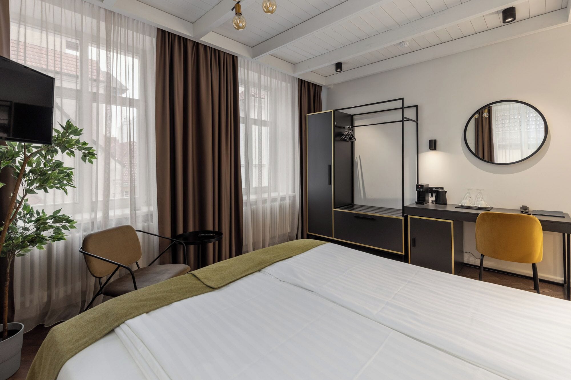 Een hotelkamer met een bed, een bureau, een stoel, een televisie, een spiegel en een potplant.