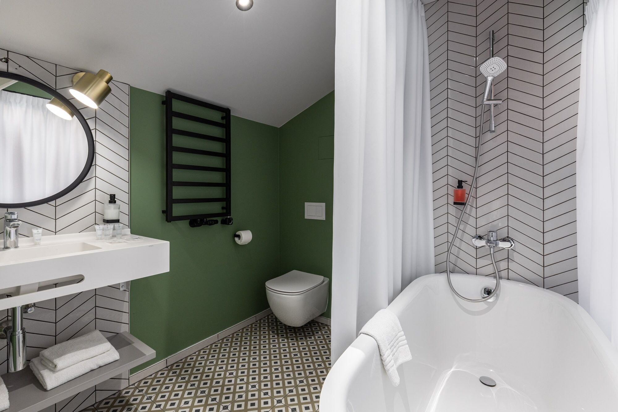 Un baño moderno con lavamanos, espejo y bañera blancos. Se observan un perchero y un inodoro.