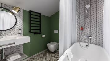 Un baño moderno con lavamanos, espejo y bañera blancos. Se observan un perchero y un inodoro.