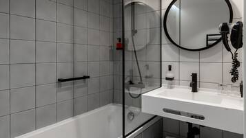 A modern bathroom with a bathtub, a glass-enclosed shower, a white sink, and a round mirror.