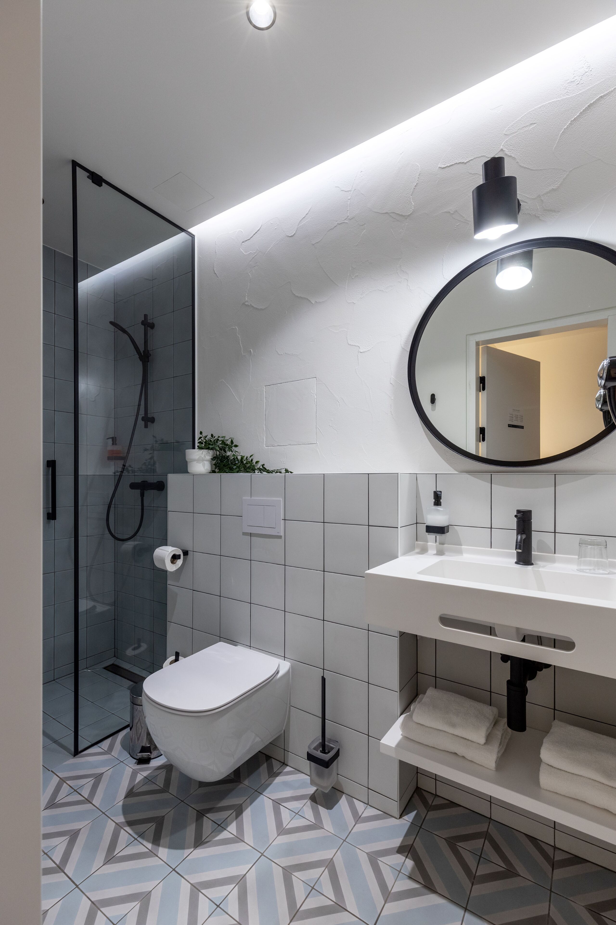 Un baño moderno con cabina de ducha de vidrio, inodoro blanco, lavamanos con espejo y suelo estampado.