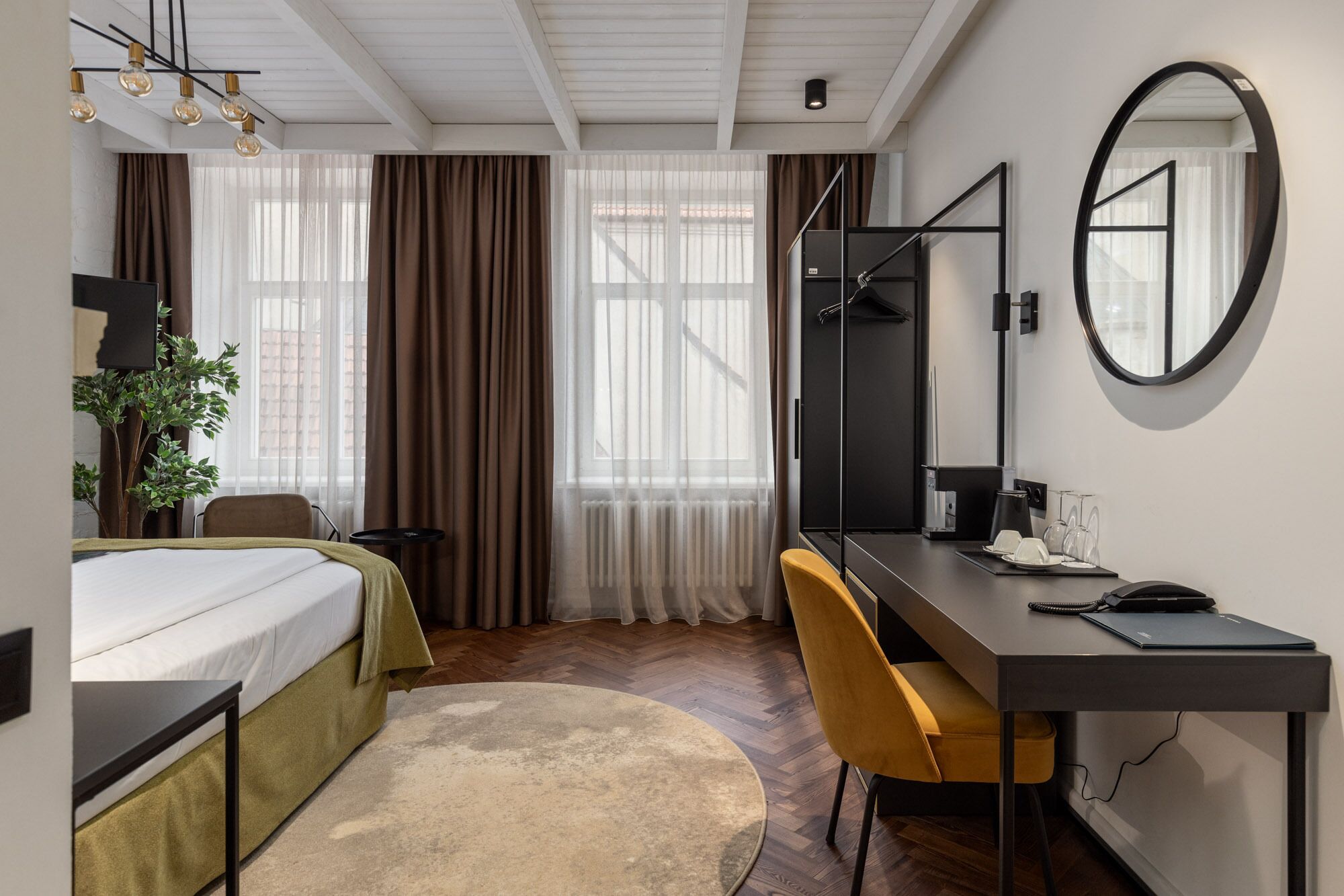 A hotel room with a bed, a desk, a chair, a mirror, and a window with curtains.