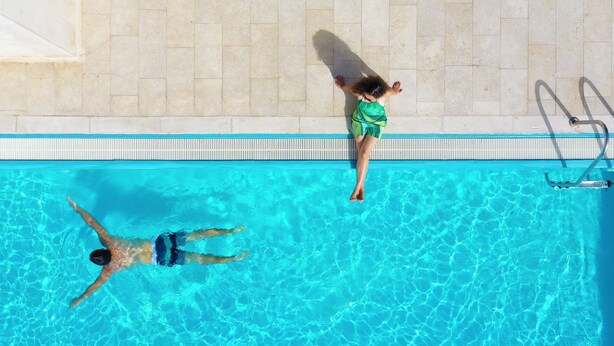Una piscina amb aigua transparent de color blau i un solàrium amb rajoles.