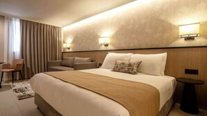 Habitació d'hotel amb un llit gran, dues làmpades de nit, una cadira i una taula petita.