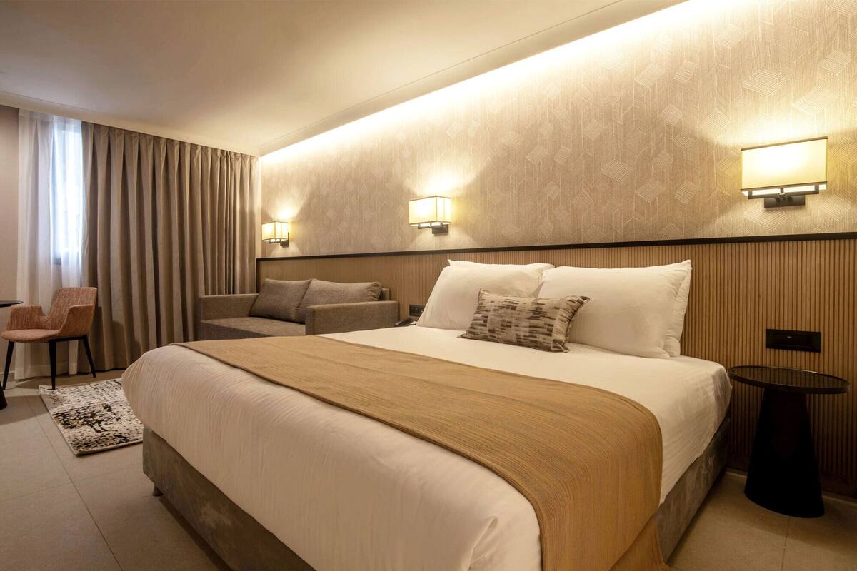 A hotel room with a large bed, two bedside lamps, a chair, and a small table.