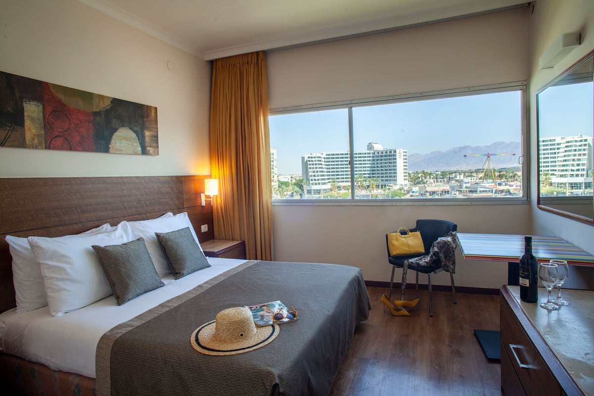 Ein Hotelzimmer mit einem großen Bett, Blick auf die Stadt, einem Schreibtisch mit Stuhl und einem Vorhangfenster.