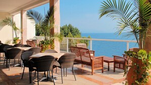An outdoor patio with wicker furniture, potted plants, and a view of the sea. - Caesar Premier Tiberias (Tiberias)