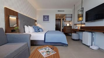 Une chambre d’hôtel moderne comprenant un lit, un canapé, une table basse en bois avec un magazine, une télévision et un bureau avec une lampe.