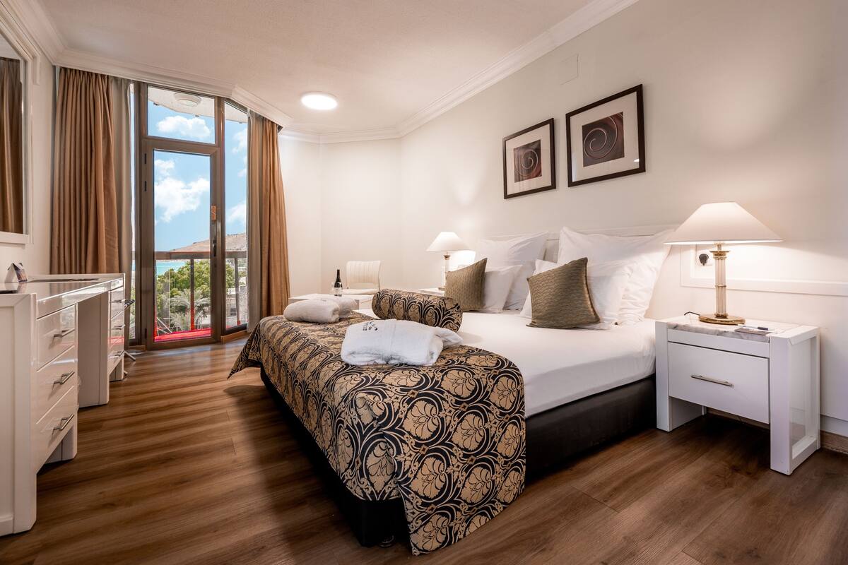 A hotel room with a large bed, two bedside tables, a desk, and a view of the outdoors.