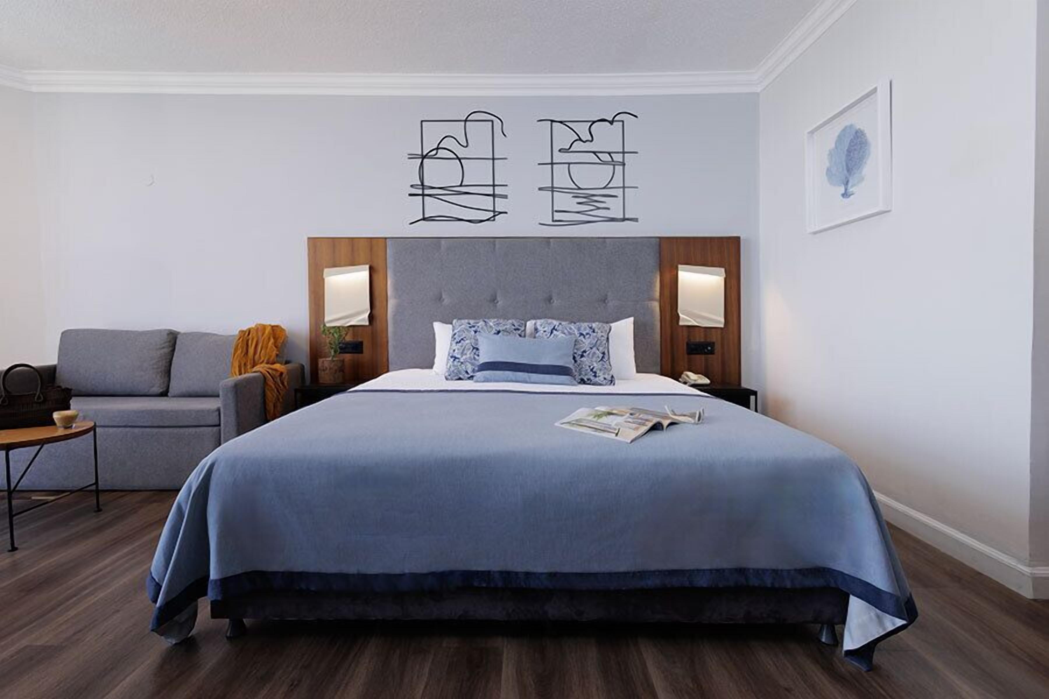 A modern hotel room with a large bed, a grey sofa, and a small table.