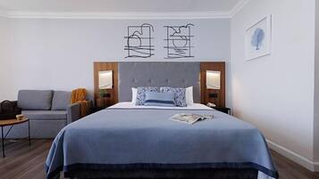 Una habitación de hotel moderna con una cama grande, un sofá gris y una mesita.