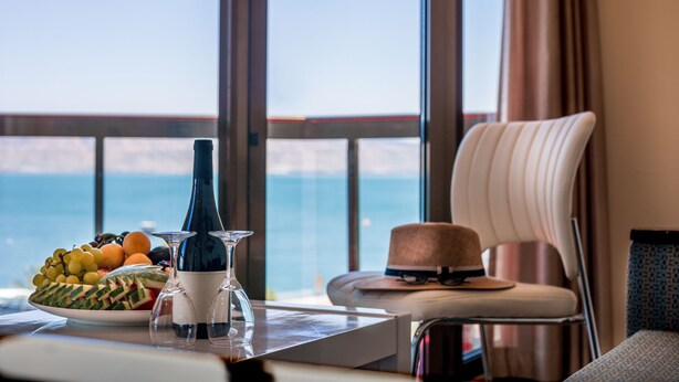 A table with a bottle, glasses, and fruit in a room with a view of the sea. - Caesar Premier Tiberias (Tiberias)